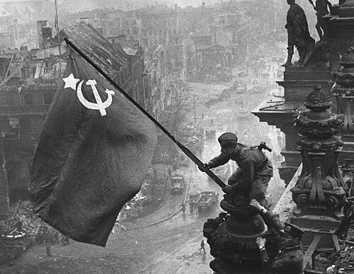 A Soviet soldier raising a flag over the ruined Reichstag building in Berlin in 1945.