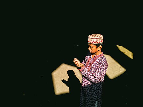 A young Muslim raising his hands in dua (supplication), eyes closed in concentration